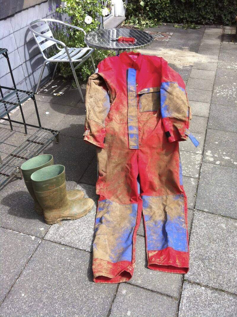 Combinaison rouge à renforts bleus couverte de boue, étalée au sol à côté d'une paire de bottes en caoutchouc