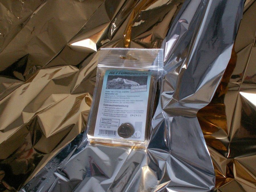 Couverture de survie dépliée, face dorée et face argentée, avec une deuxième couverture encore pliée dans son sachet plastique