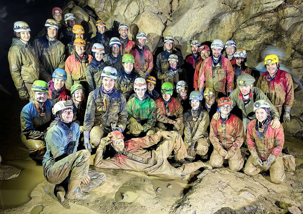 Groupe d'une école de spéléologie dans une salle boueuse : chaque casque porte une lampe frontale électrique