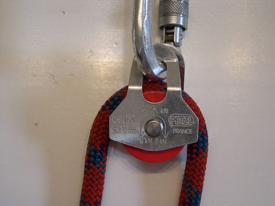 Petite poulie Petzl à flasques mobiles, une corde rouge passée sur le réa, suspendue à un mousqueton à vis