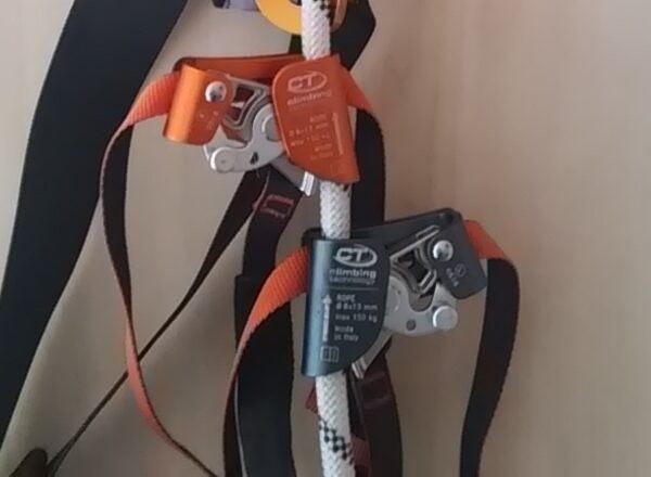Deux bloqueurs de pied Climbing Technology sur une corde blanche, l'un orange, l'autre gris, avec leurs sangles de fixation à la botte
