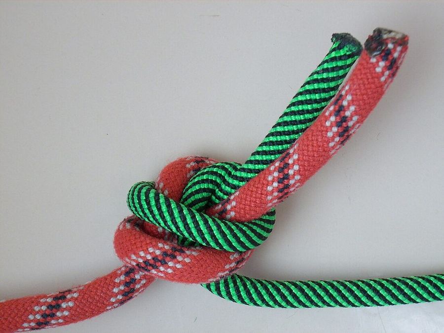 Une corde rouge et une verte nouées ensemble par un nœud simple, les deux bouts libres parallèles en haut à droite